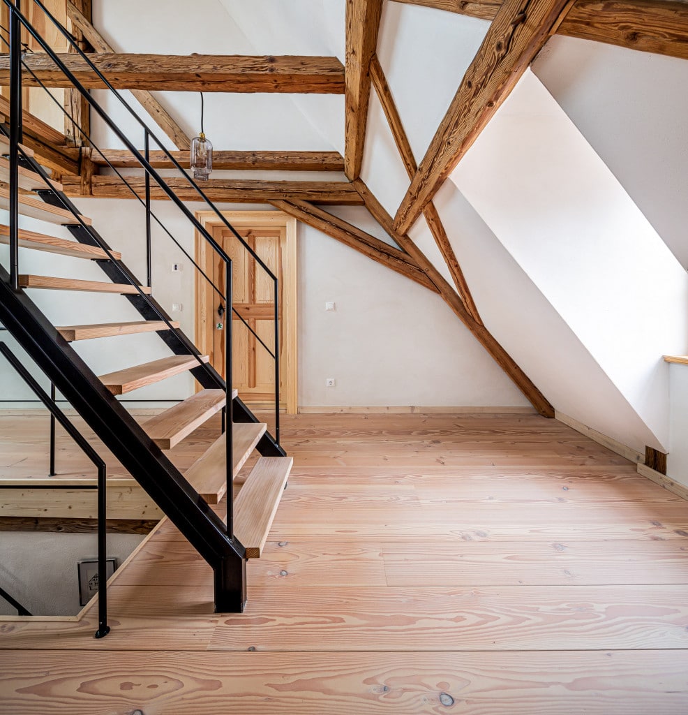 Wohnraum mit Holzbalken, schwarzer Treppe und Holzboden