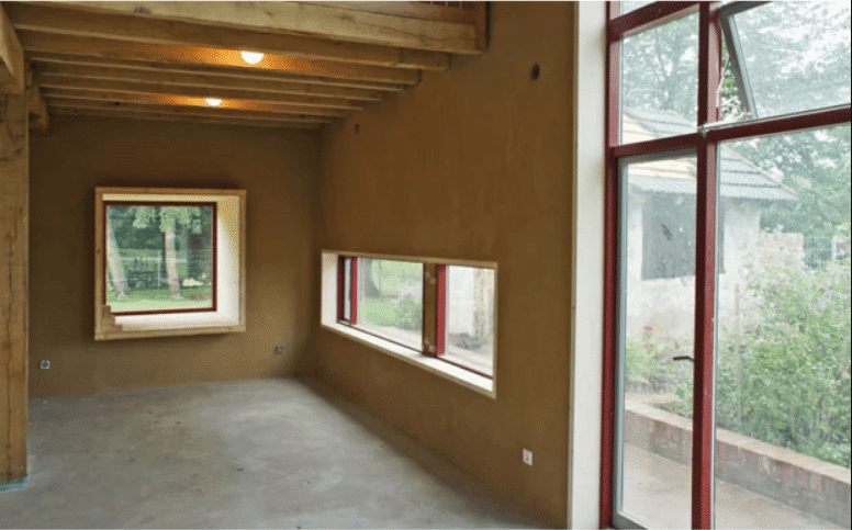 Wohnraum mit großen Fenstern, Holzbalken an der Decke und Lehmputz an den Wänden